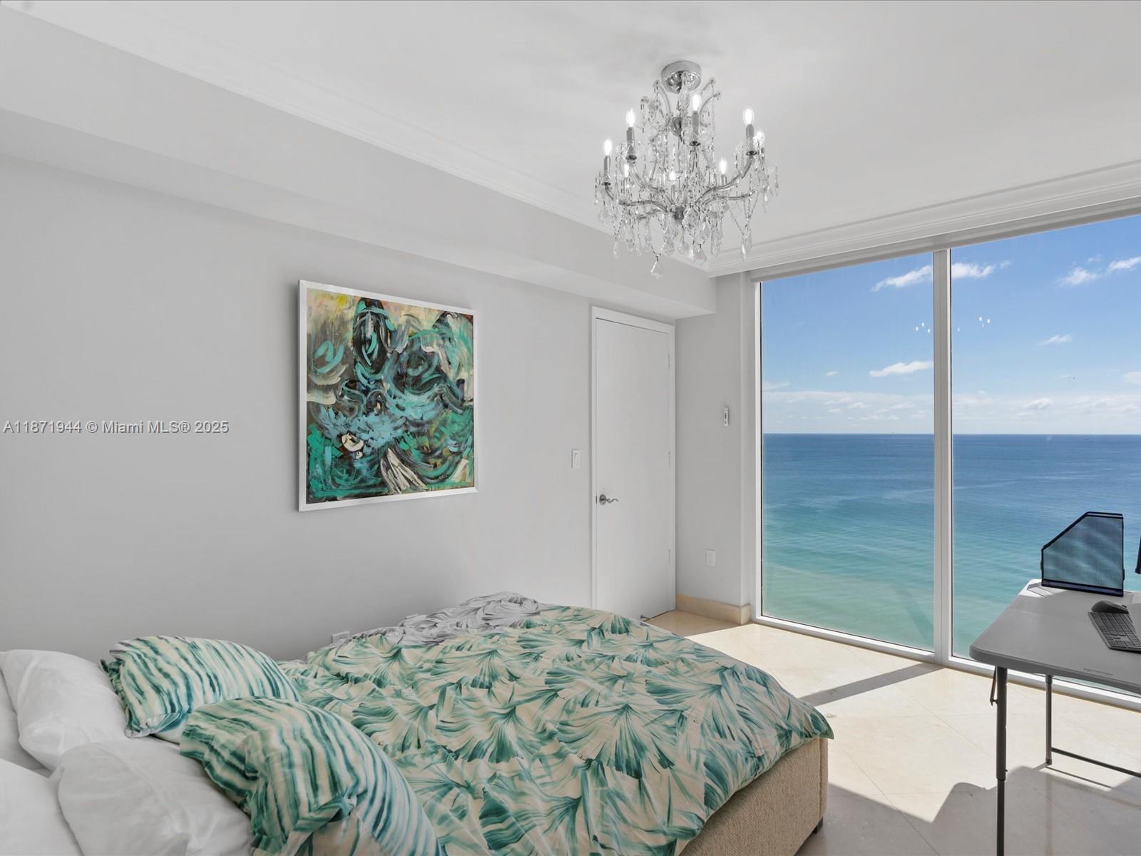 19111 Collins Avenue, Unit 1406 Sunny Isles Beach, FL 33160 - Photo 27 of 40 a bedroom with a bed chandelier and a window