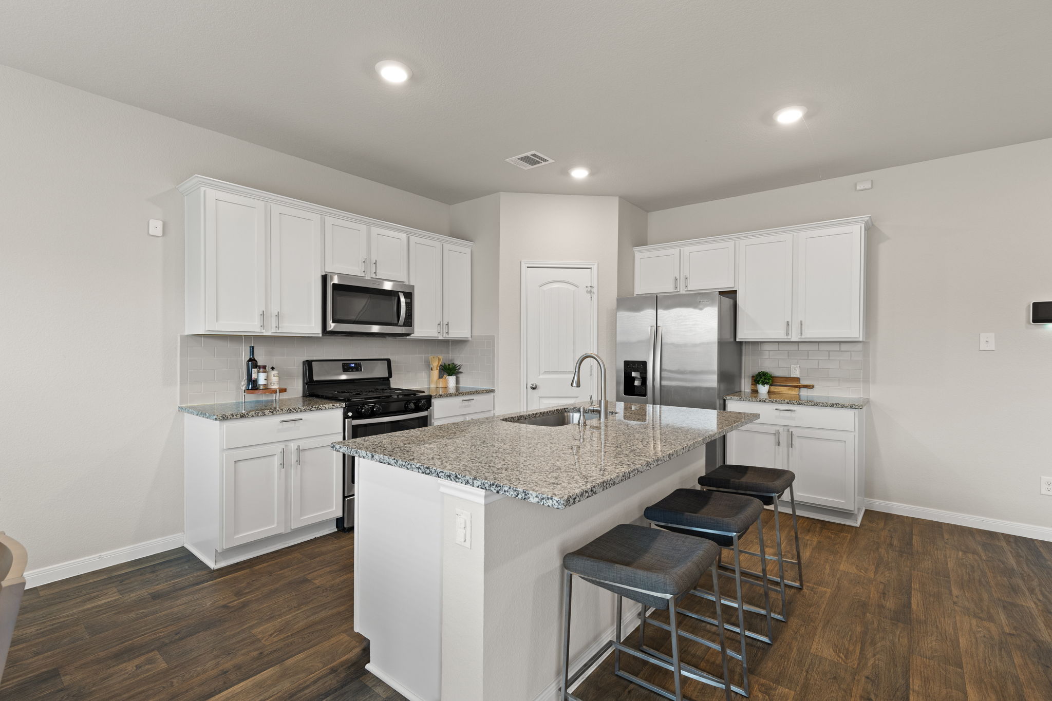 281 Jayden Drive Kyle, TX 78640 - Photo 12 of 36 Open-concept kitchen featuring an island with a built-in sink, stainless steel appliances, white shaker cabinetry, and wood-finish flooring
