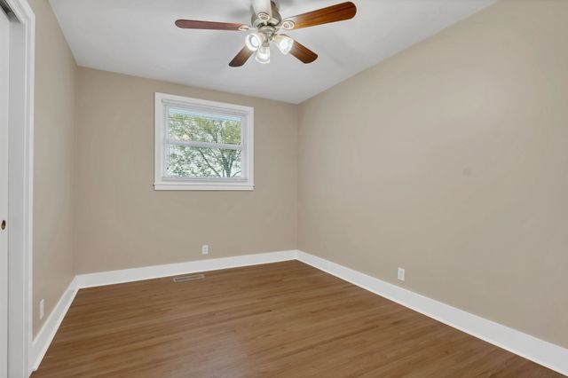 an empty room with wooden floor chandelier fan and windows