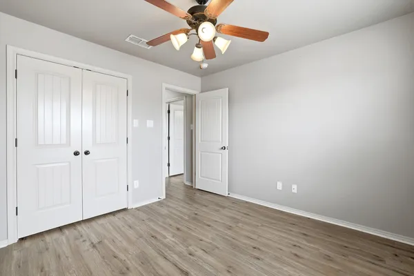 a view of an empty room with window a chandelier fan and wooden floor