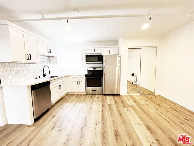 a large kitchen with a refrigerator a stove top oven a sink dishwasher and white cabinets with wooden floor