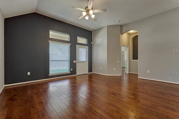 an empty room with wooden floor chandelier fan and windows