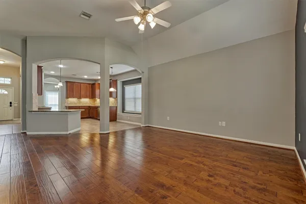 a view of an empty room with wooden floor and a kitchen