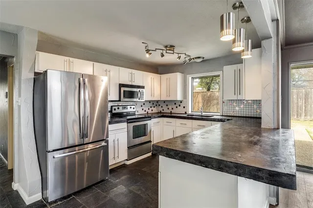a large kitchen with granite countertop a refrigerator a stove and white cabinets