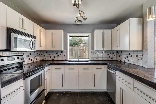 a kitchen with granite countertop white cabinets white stainless steel appliances a sink and a window