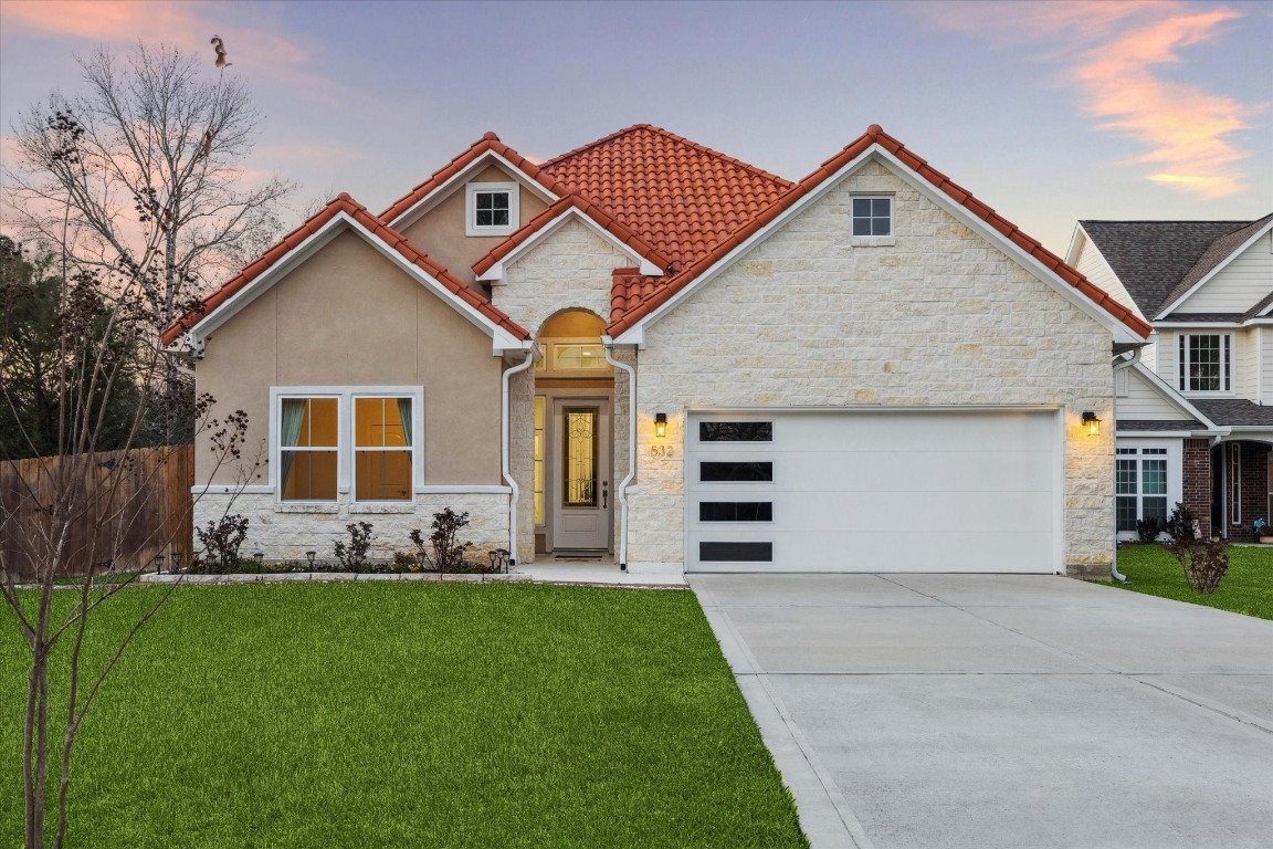 532 Carrell Street Tomball, TX 77375 - Photo 2 of 28 Beautifully designed modern home featuring a striking blend of stone and stucco exterior, complemented by a bold red tile roof that adds distinctive character and curb appeal. This single-story residence showcases a welcoming covered entry with elegant architectural details and warm exterior lighting.