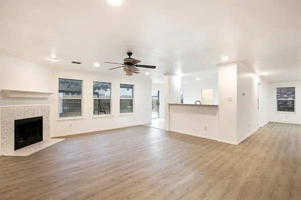 a view of an empty room with wooden floor and a kitchen
