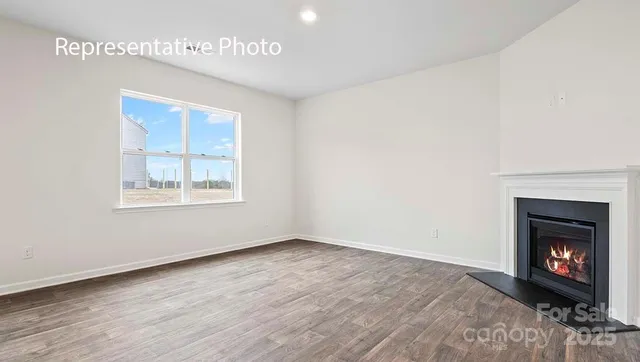 a view of an empty room with wooden floor a fireplace and a window