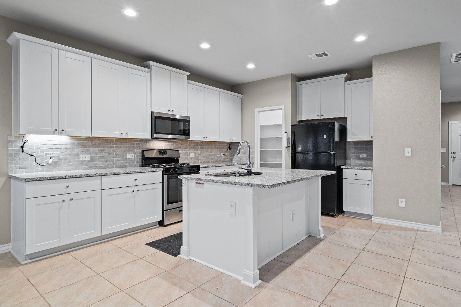 204 Tulum Terrace Leander, TX 78641 - Photo 10 of 22 Kitchen featuring stainless steel appliances, white cabinetry, light tile patterned floors, a kitchen island with sink, and recessed lighting