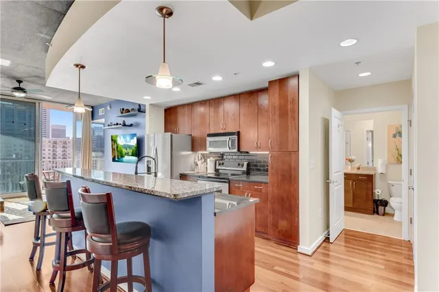 a kitchen with stainless steel appliances kitchen island granite countertop a refrigerator oven a sink dishwasher a dining table and chairs with wooden floor