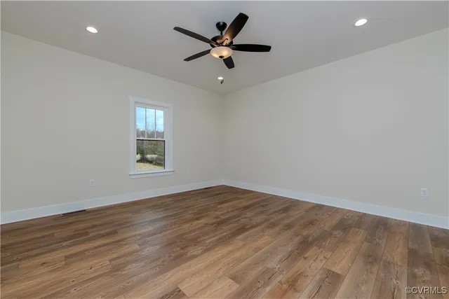 an empty room with wooden floor fan and windows