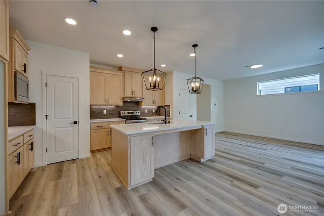 a large kitchen with granite countertop a stove a sink dishwasher a refrigerator white cabinets and wooden floor next to a window