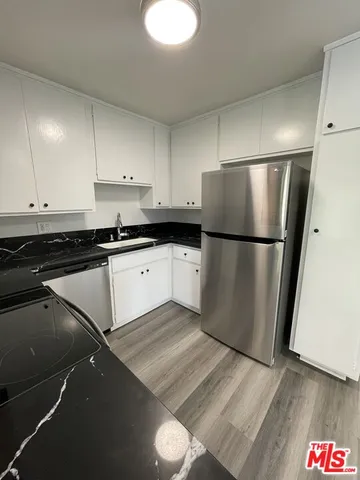 a kitchen with granite countertop a refrigerator a sink and white cabinets