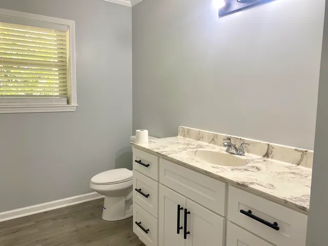 a bathroom with a granite countertop toilet a sink and a window