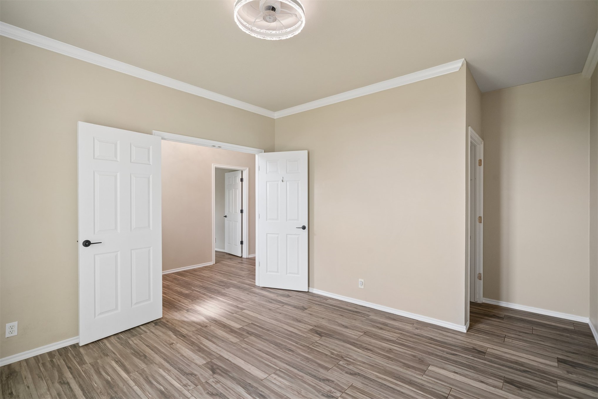Wood-finish flooring, crown molding, neutral wall color, recessed lighting, and paneled doors