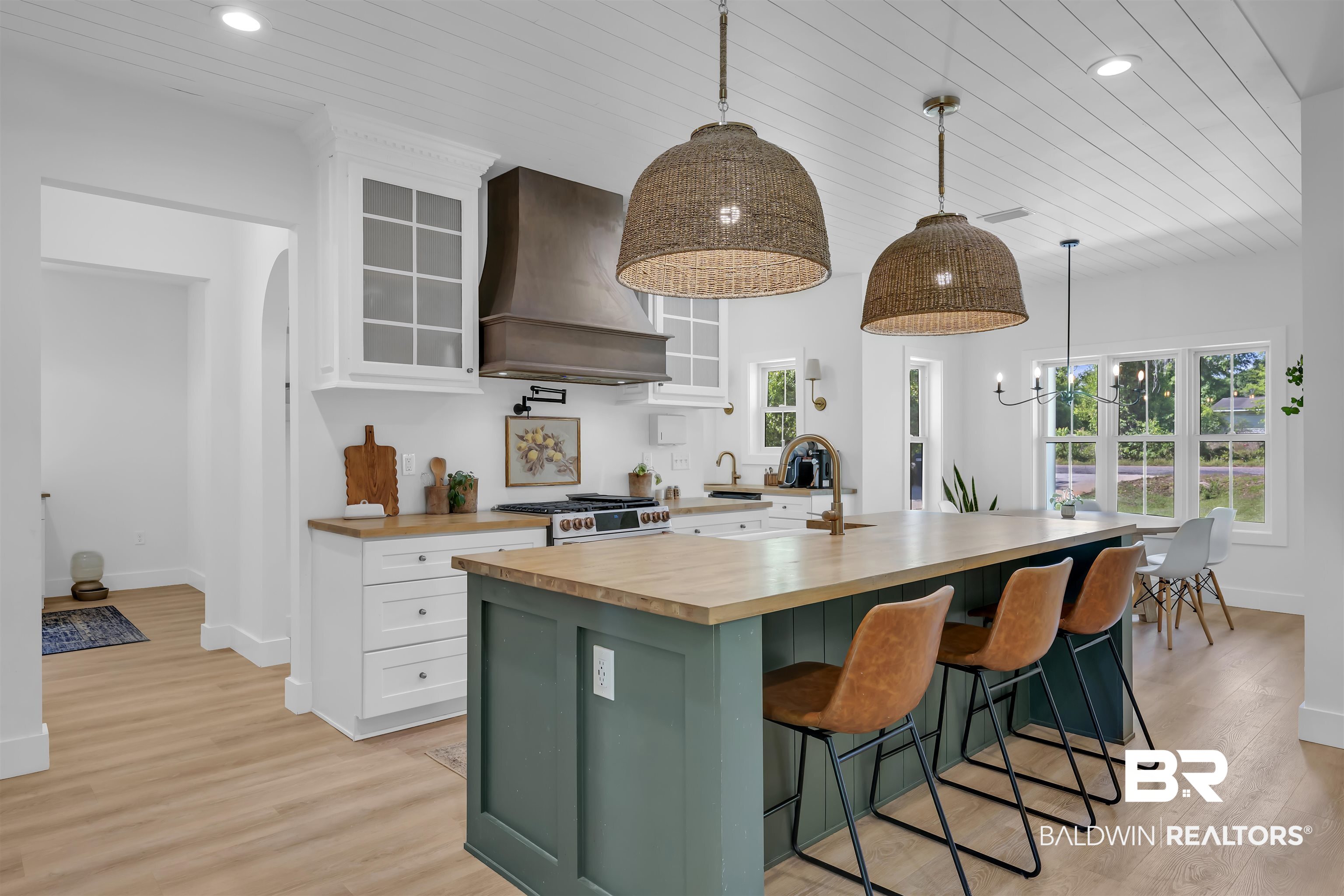 19058 James Road Gulf Shores, AL 36542 - Photo 14 of 49 Two tone kitchen featuring two tone cabinets, glass fronted cabinets, butcher block counters, a kitchen bar, and an island with sink