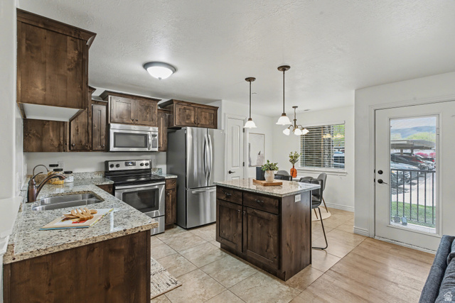 861 South Main Street, Unit D Layton, UT 84041 - Photo 1 of 1 Kitchen with dark wood finish cabinets, stainless steel appliances, light stone countertops, a kitchen island, and light tile patterned floors