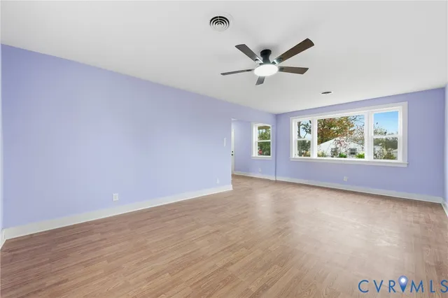 an empty room with wooden floor fan and windows