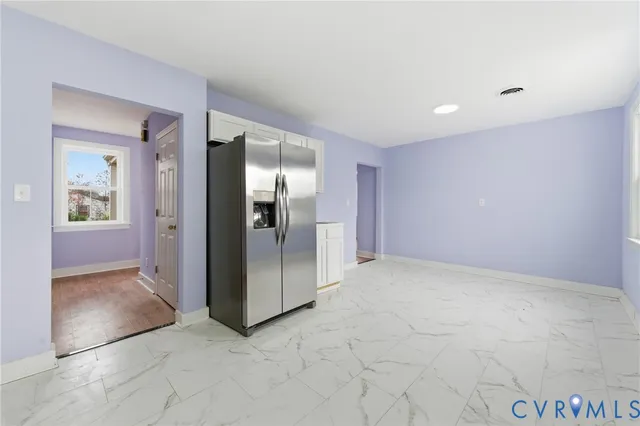 an empty room with kitchen view and refrigerator