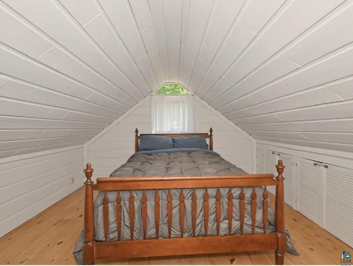 88440 Huron Street Cornucopia, WI 54827 - Photo 21 of 44 Attic room featuring sloped, white wood-paneled walls and ceiling, natural wood-finish flooring, and built-in louvered storage units. It can be used for an office, a game room, or extra storage.