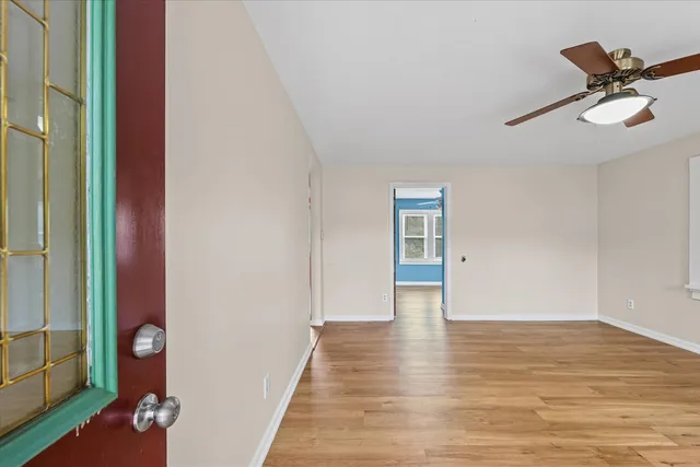 a view of an empty room with wooden floor and a ceiling fan