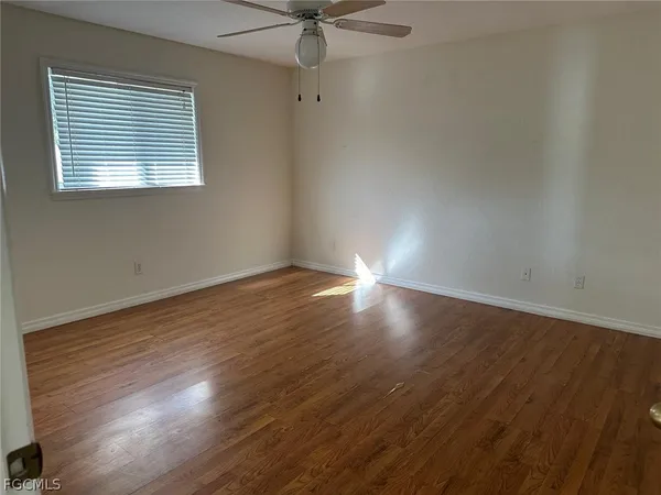 an empty room with wooden floor fan and windows