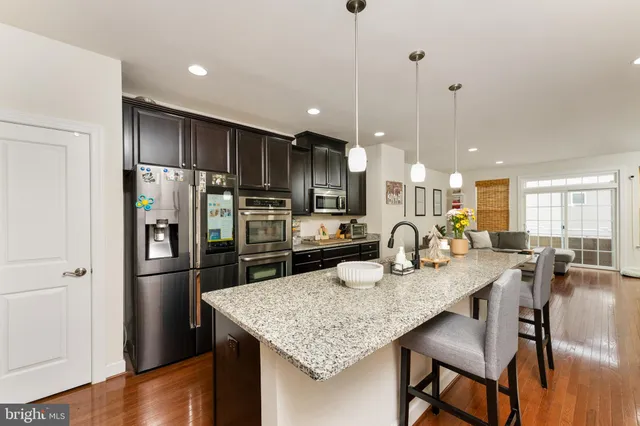 a kitchen with stainless steel appliances granite countertop a refrigerator a stove a sink a dining table and chairs with wooden floor