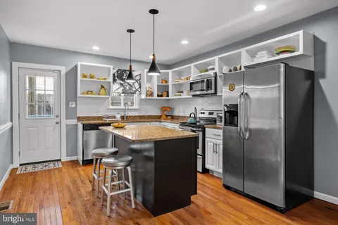 a kitchen with stainless steel appliances granite countertop a refrigerator a sink dishwasher a stove and a dining table with wooden floor