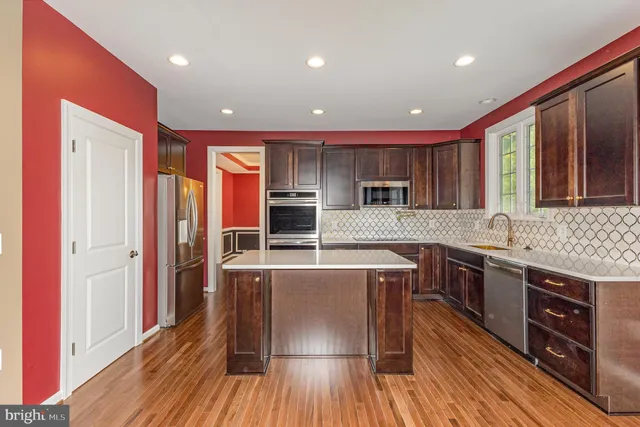 a kitchen with stainless steel appliances granite countertop a refrigerator a sink dishwasher a stove and white countertops with wooden floor