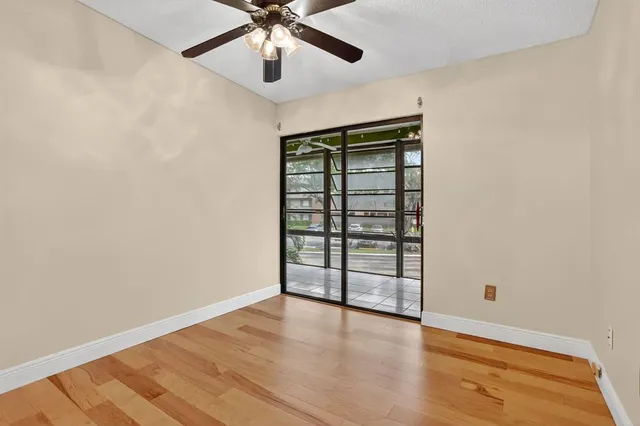 an empty room with wooden floor chandelier fan and windows