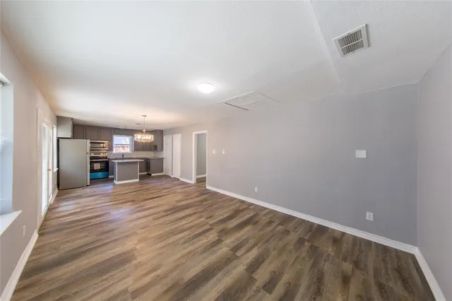 a view of empty room with wooden floor and kitchen view