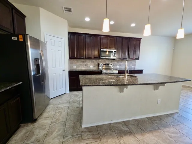 a kitchen with stainless steel appliances granite countertop a refrigerator a sink a stove a microwave and wooden cabinets