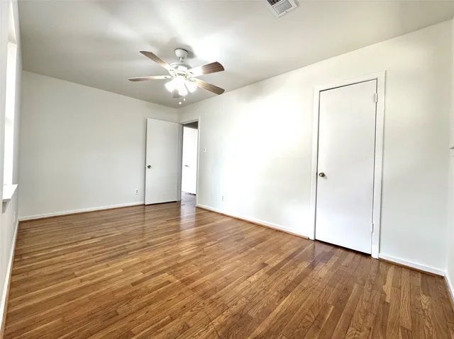 an empty room with wooden floor fan and windows