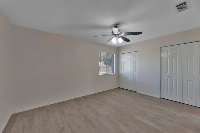 an empty room with wooden floor ceiling fan and windows