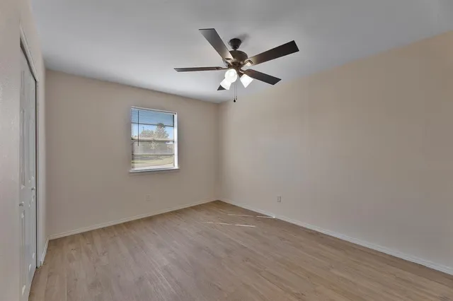 a view of an empty room with wooden floor and a ceiling fan