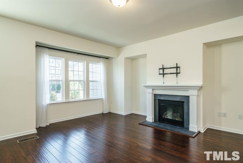 4956 Highcroft Drive Cary, NC 27519 - Photo 7 of 17 an empty room with wooden floor fireplace and windows