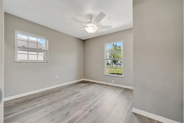 an empty room with wooden floor chandelier fan and windows