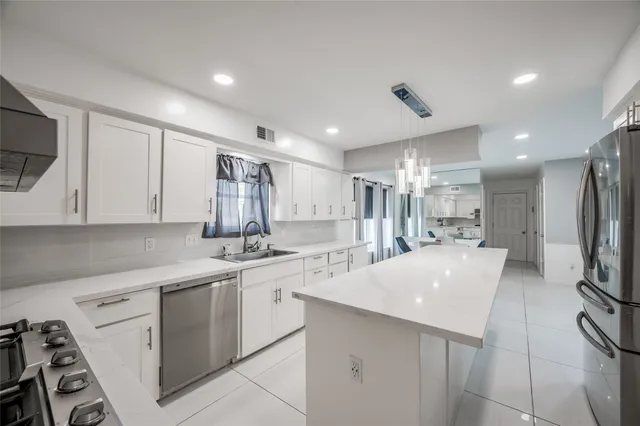 a large white kitchen with stainless steel appliances kitchen island a white counter space a sink and a refrigerator