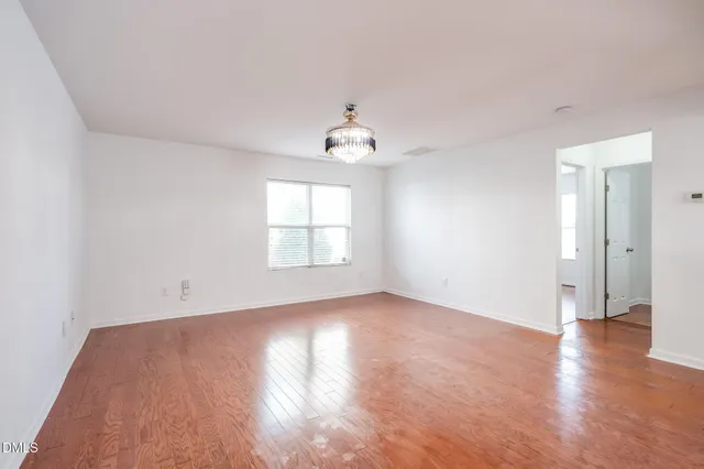 an empty room with wooden floor chandelier and windows