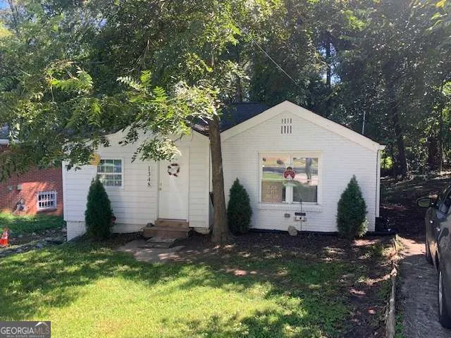a view of a white house with a small yard and large tree
