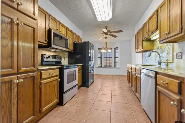 a large kitchen with stainless steel appliances granite countertop a stove top oven a sink dishwasher and a refrigerator with wooden cabinets