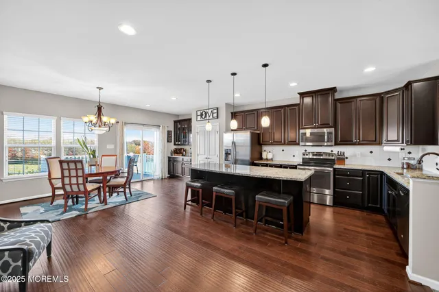 a kitchen with stainless steel appliances granite countertop a stove top oven a refrigerator a sink and a dining table with wooden floor