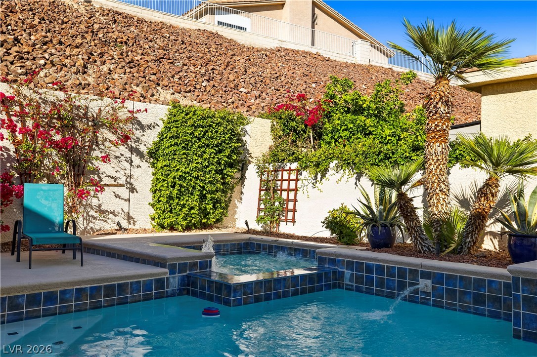 1135 Calico Ridge Drive Henderson, NV 89011 - Photo 52 of 86 A tranquil oasis awaits, complete with a sparkling pool, spa, and mature landscaping against a rugged hillside backdrop.