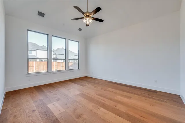 an empty room with wooden floor fan and windows