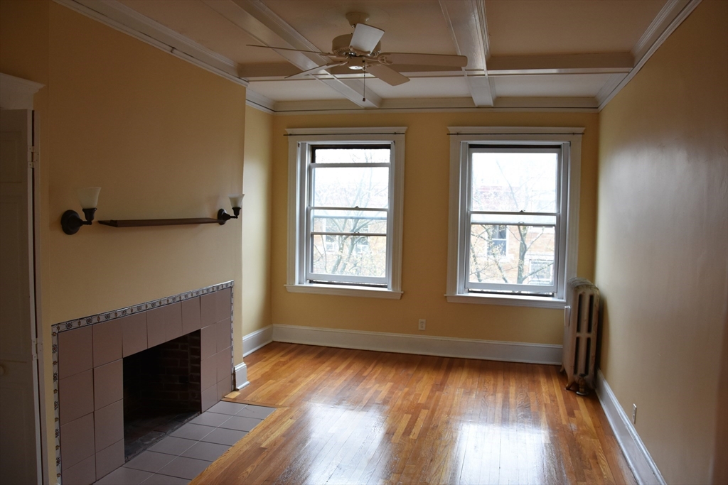 134 Fuller Street, Unit 3 Brookline, MA 02446 - Photo 5 of 8 a view of an empty room with wooden floor fireplace and a window