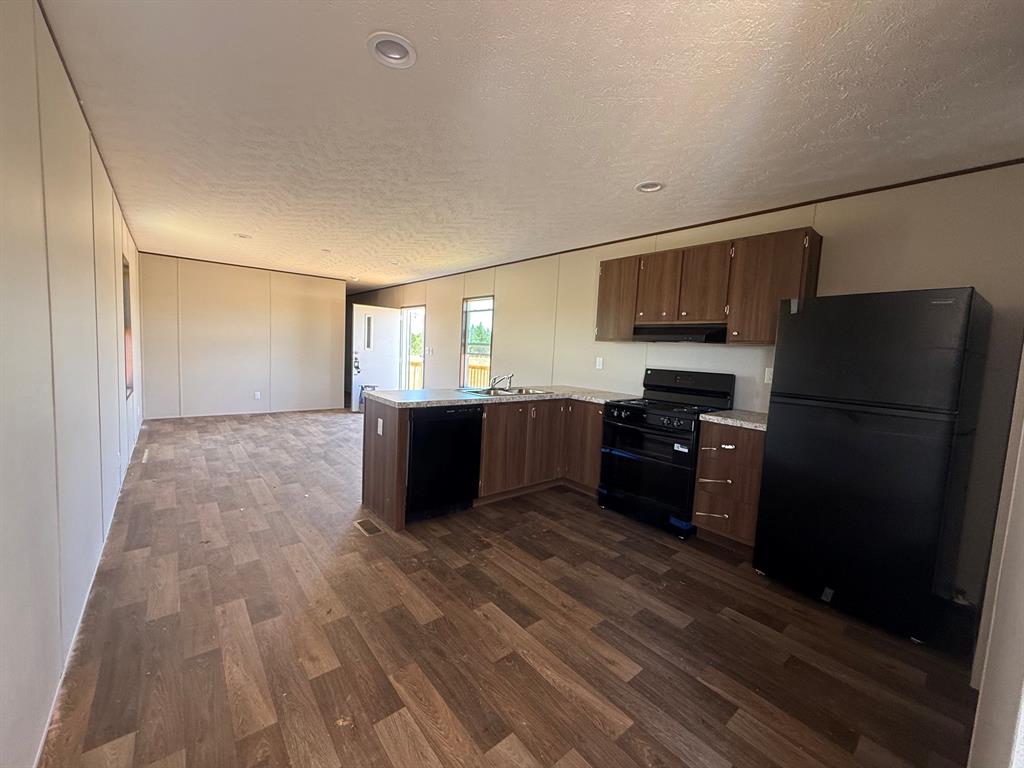 0 Southeast 4060 Road, Unit 25 Kerens, TX 75144 - Photo 8 of 18 Open-concept kitchen featuring wood-finish cabinetry, black appliances including a refrigerator, stove, and dishwasher, and light-toned countertops