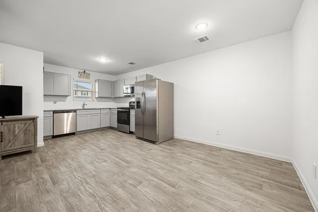a view of kitchen with stainless steel appliances granite countertop a stove top oven a sink dishwasher and a refrigerator with wooden floor