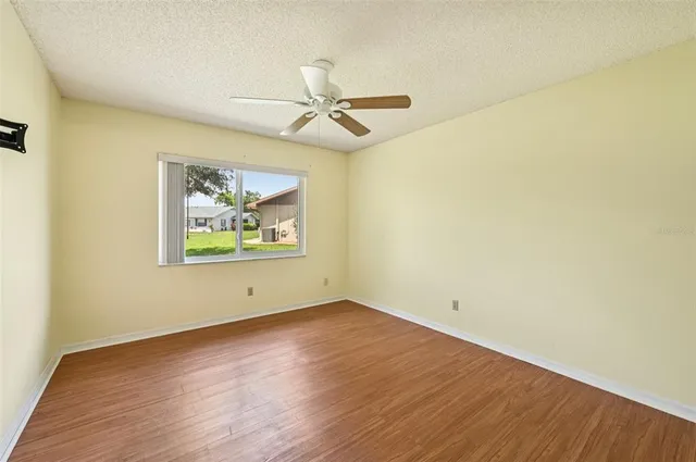 an empty room with wooden floor ceiling fan and window