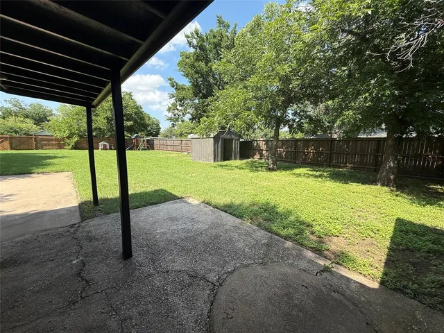 a view of a backyard with table and chairs under an umbrella with large trees