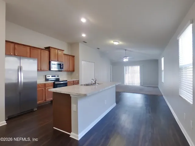 a kitchen with stainless steel appliances granite countertop a refrigerator a sink dishwasher a stove and white countertops with wooden floor